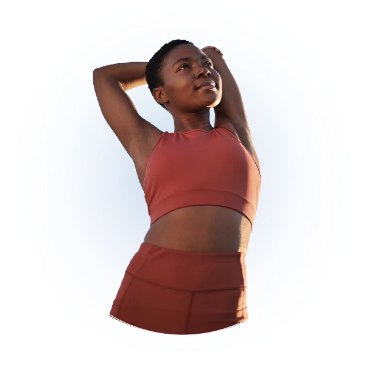 Person in burgundy athletic crop top and skirt stretches arms overhead against white background
