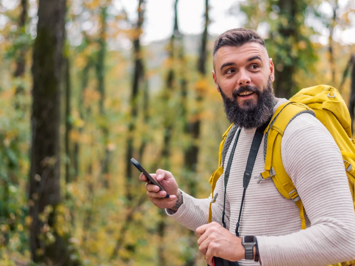 Person in white shirt with yellow backpack holds mobile phone on outdoor trail