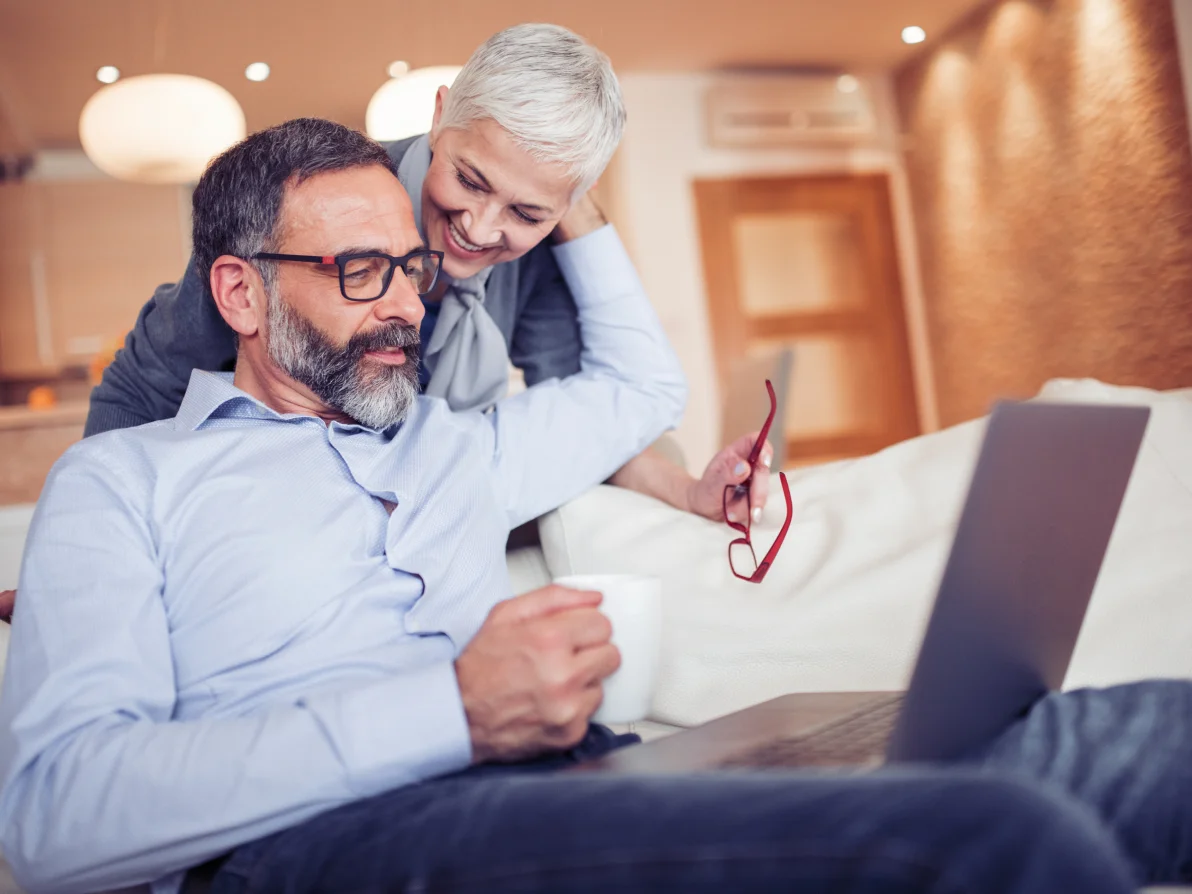 Two people look at laptop, one in light blue button-up shirt with black glasses, one in gray blazer holding red eyeglasses