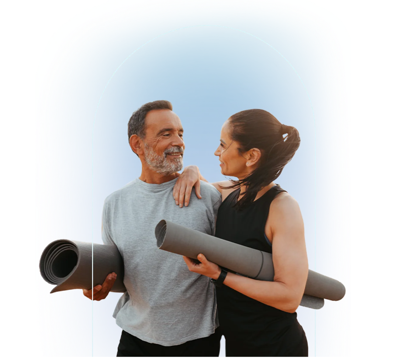 Two people standing together holding rolled gray yoga mats, one wearing light gray t-shirt with black pants and one wearing black sleeveless top with black pants