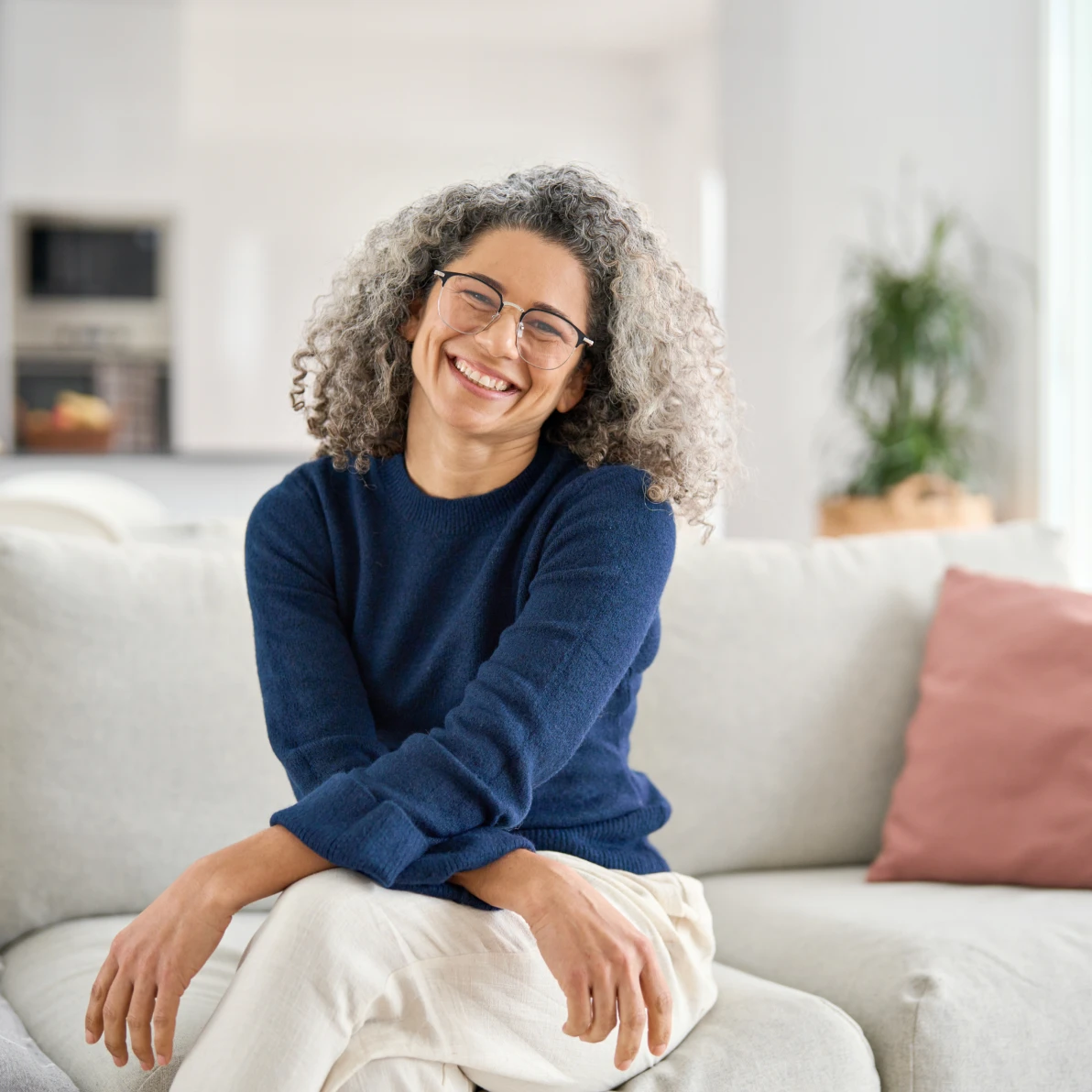 Person in navy blue sweater sitting on beige couch with pink pillow visible