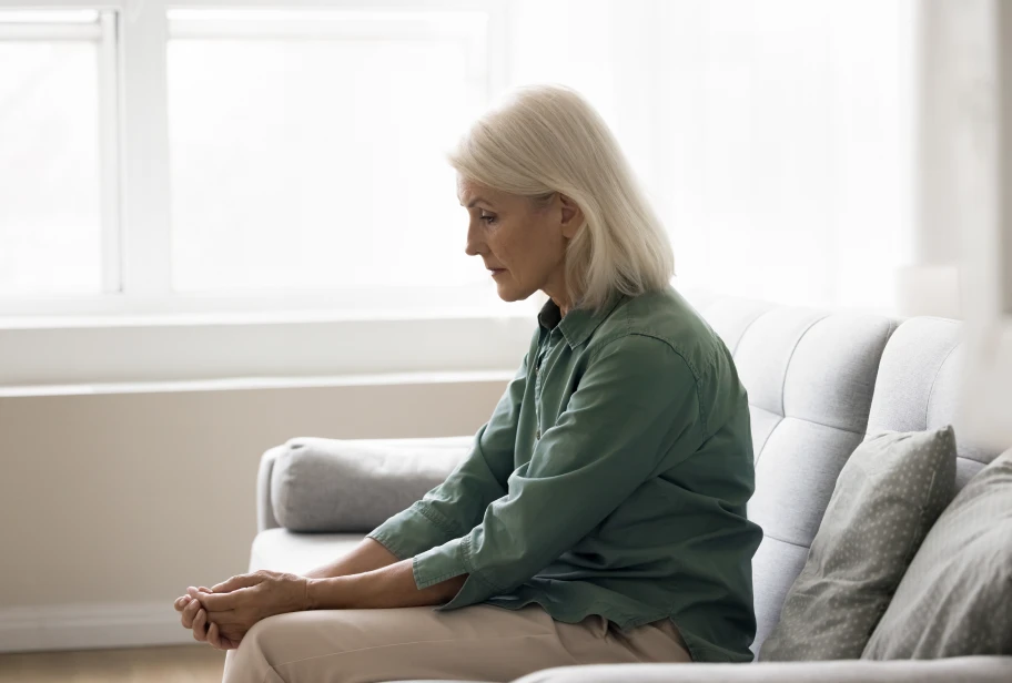 Person in green long-sleeve shirt sitting on light gray couch near window in bright room