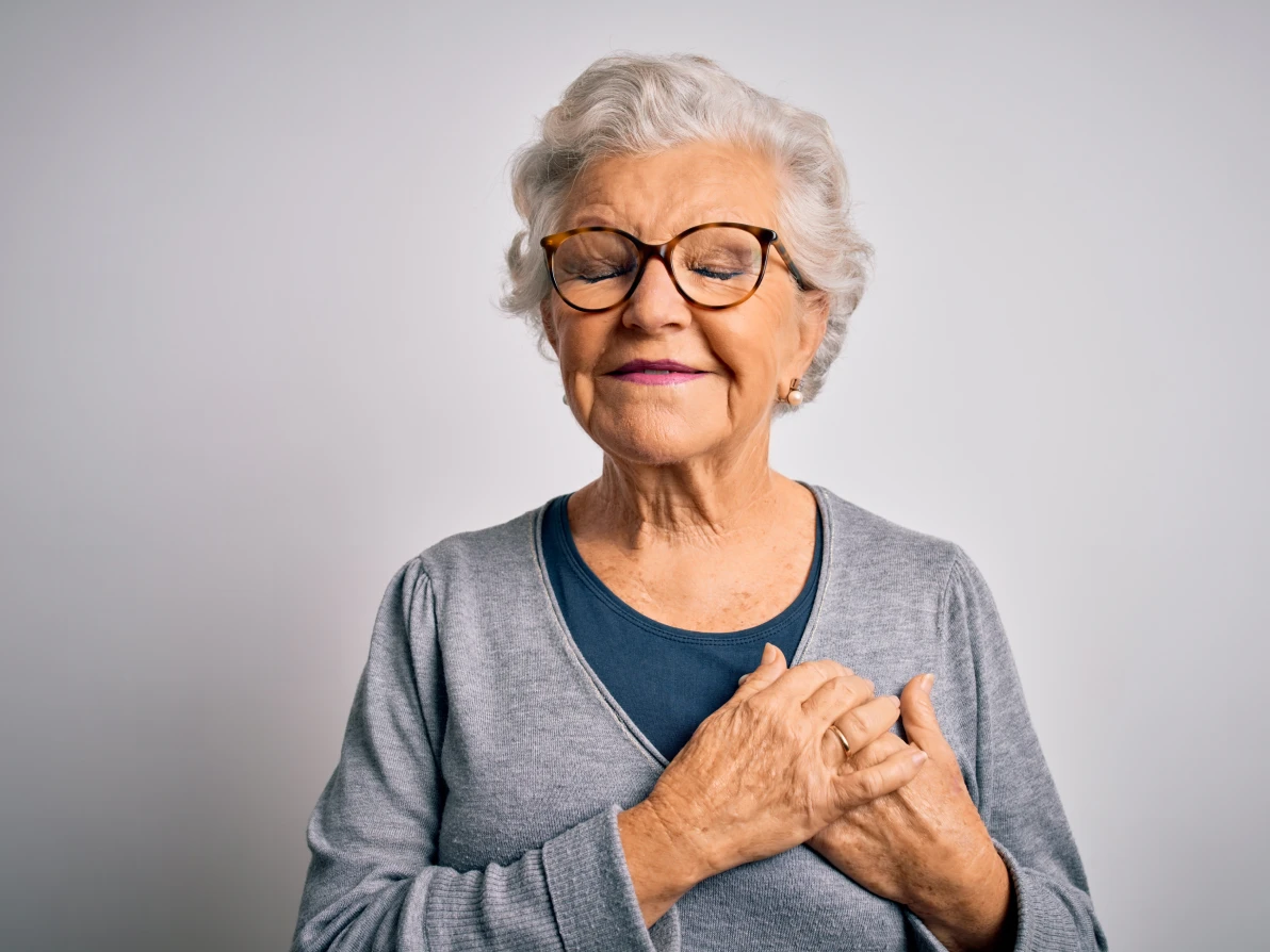 Person in gray cardigan and blue top with hands on chest