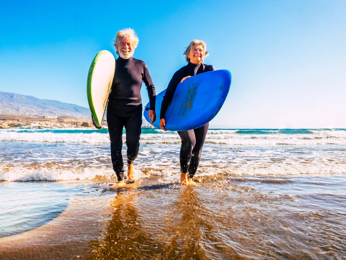 Two people in wetsuits holding surfboards while walking on a beach