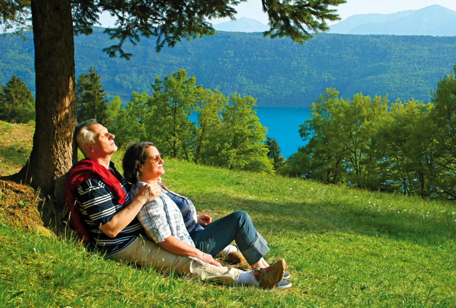 Two people sit on green grass with mountain range visible in background