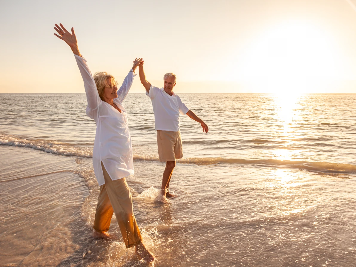 Two people with arms raised high on beach at sunset or sunrise with ocean and golden sunlight in background