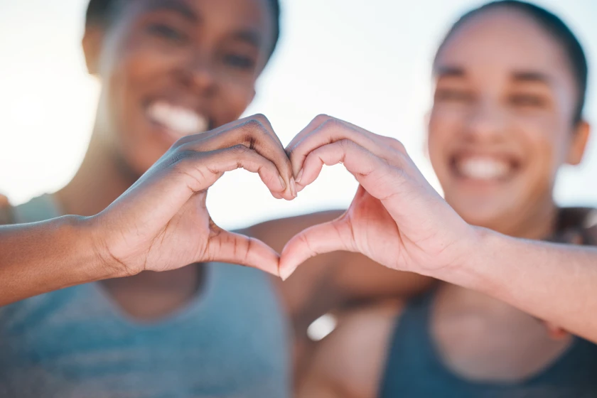 Two sets of hands forming heart shape with blurred faces in background