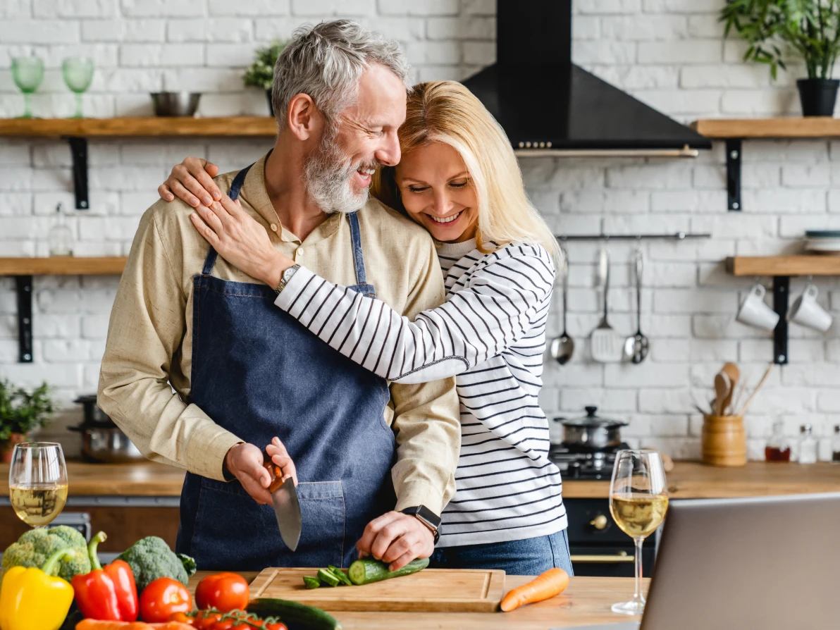 Two people preparing vegetables in kitchen, one wearing blue apron and one wearing striped top, with fresh produce on counter