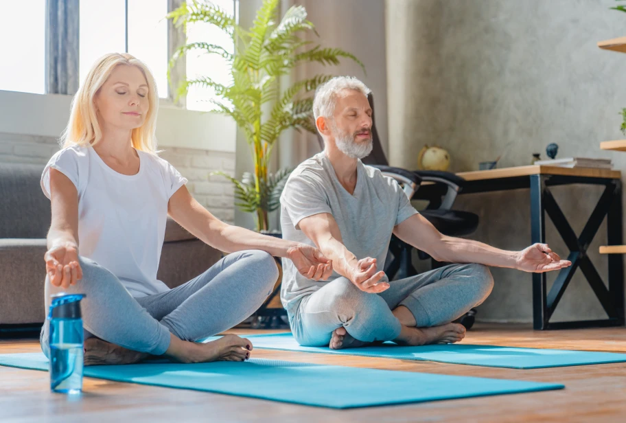 Two people sitting on blue yoga mats indoors with plants visible in background